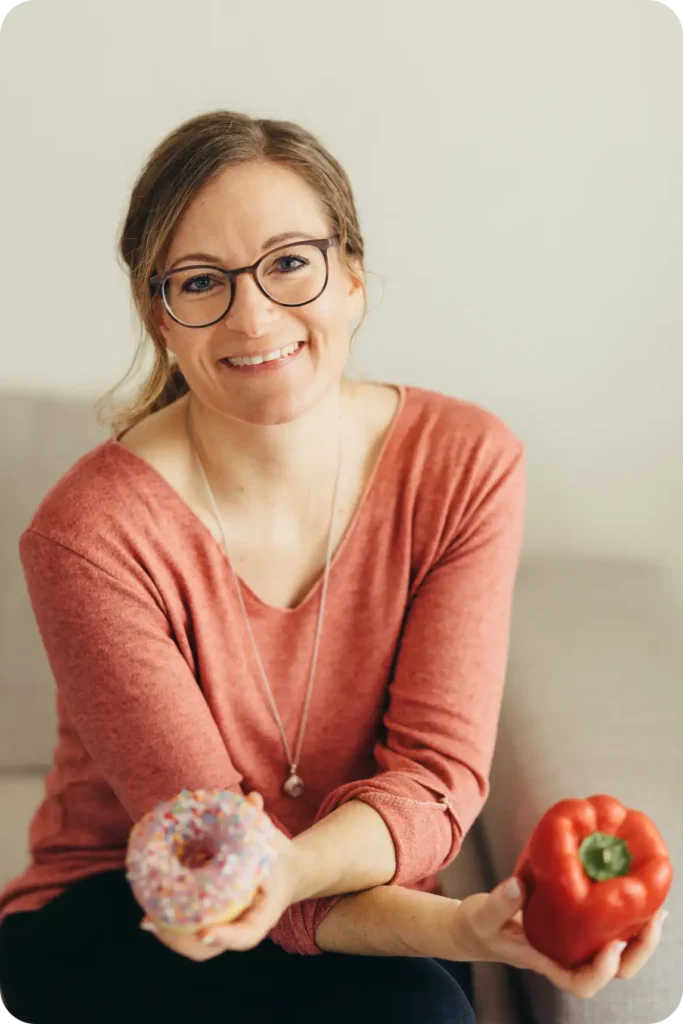 Psychologische Ernährungsberaterin, die lächelnd einen Donut und eine Paprika hält